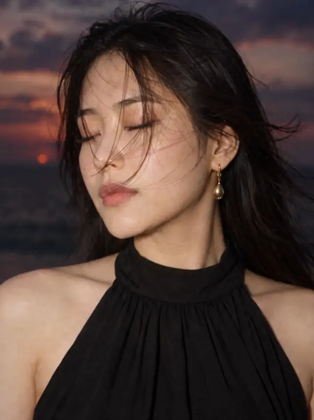夕暮れの海辺で黒いドレスを着た女性の髪が風になびく姿